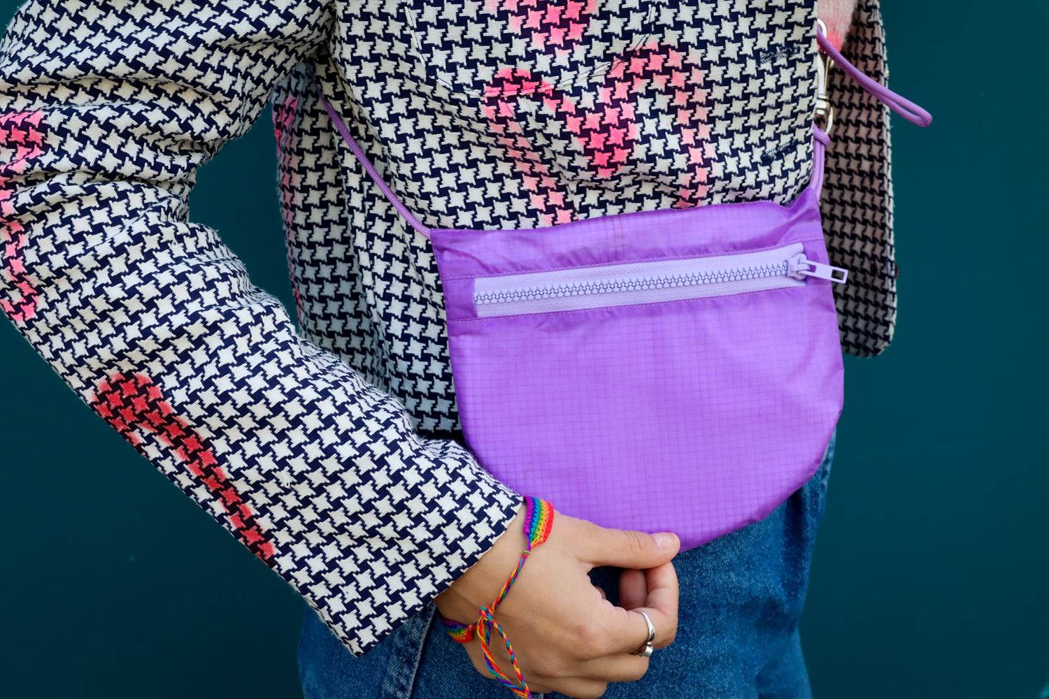 Model wearing sling bag infront of street art bag is lavender made from recycled rip stop nylon