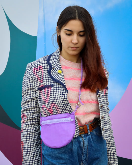 Model wearing sling bag infront of street art bag is lavender made from recycled rip stop nylon