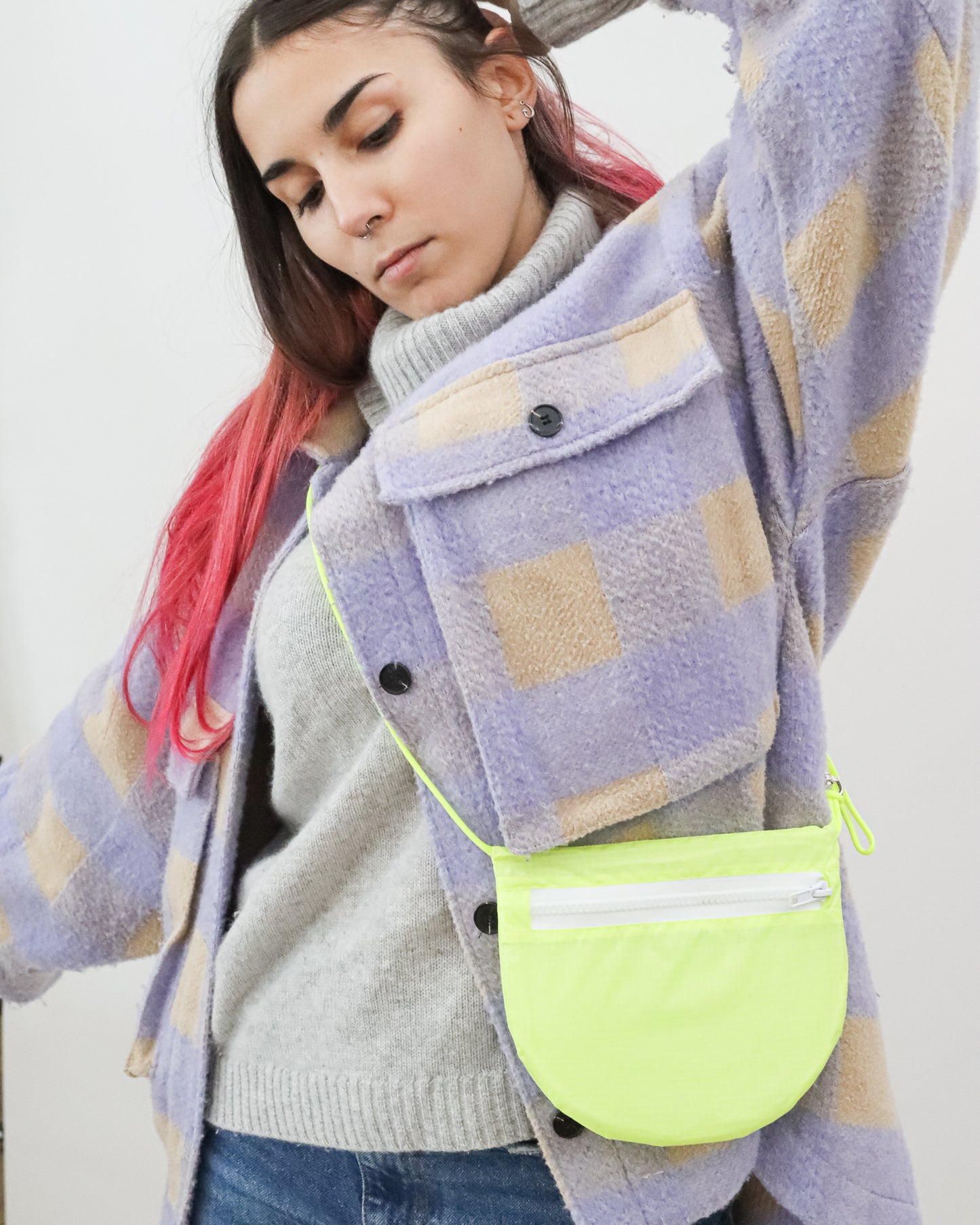Model wearing crossbody bag in neon yellow and white made from recycled ripstop nylon