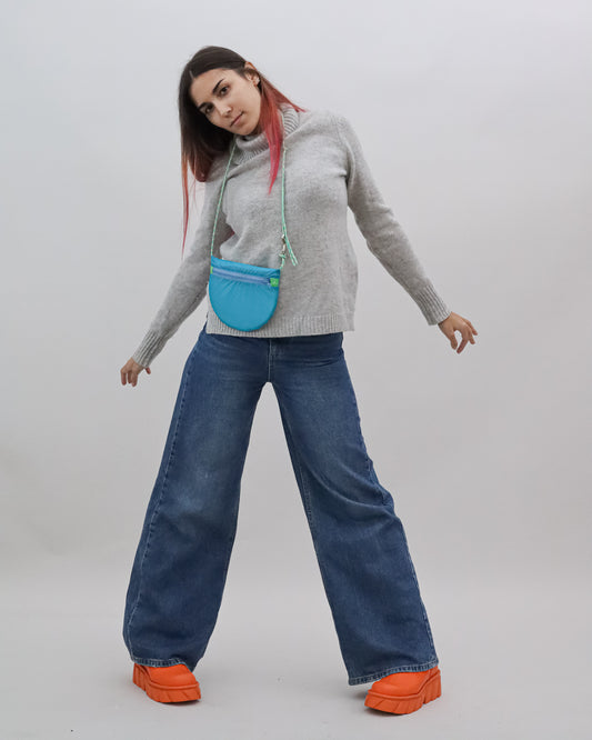 Model wearing crossbody bag in turquoise and green made from recycled rip stop nylon