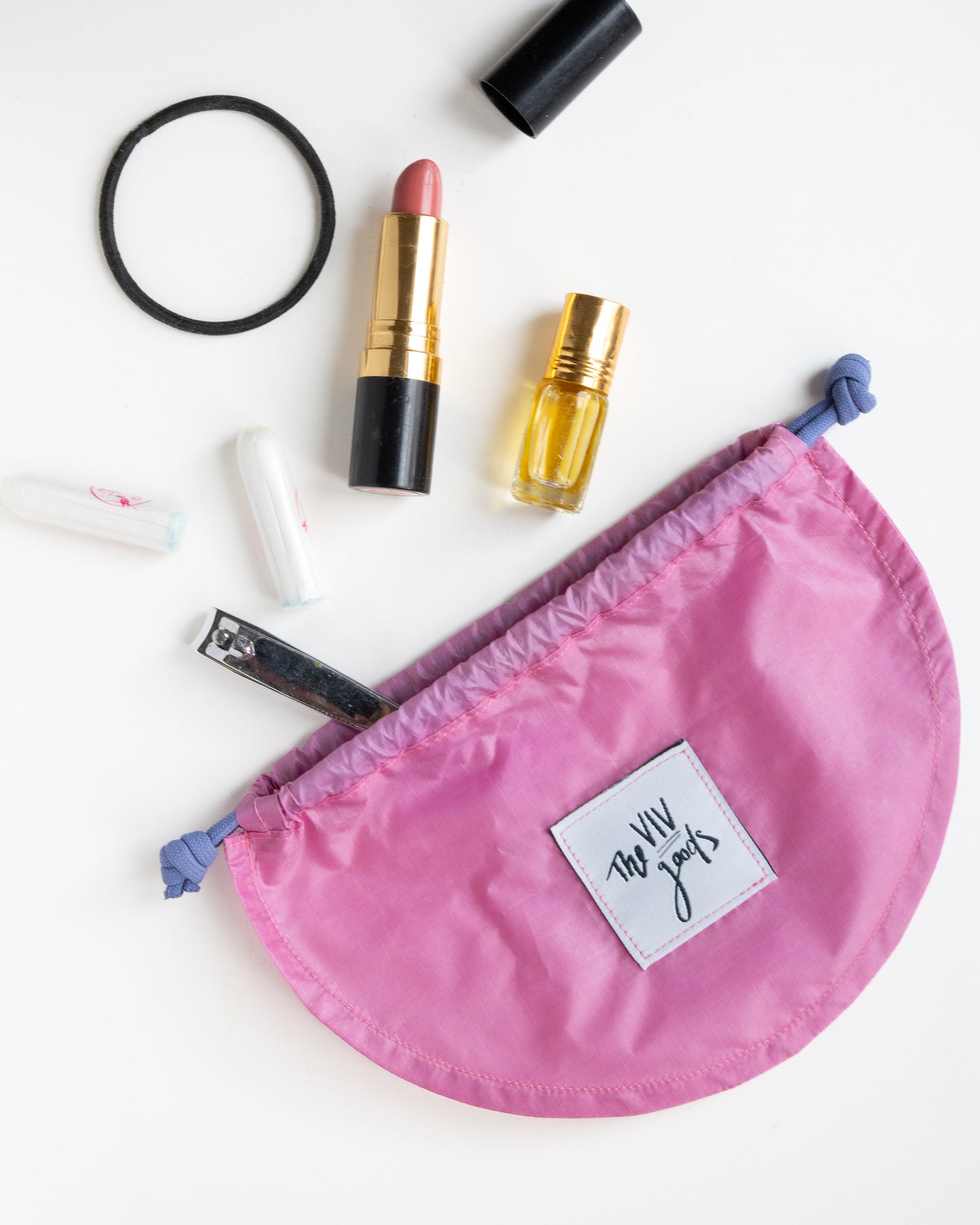 flat lay of drawstring pouch in light pink and purple with accessories that can fit inside bag