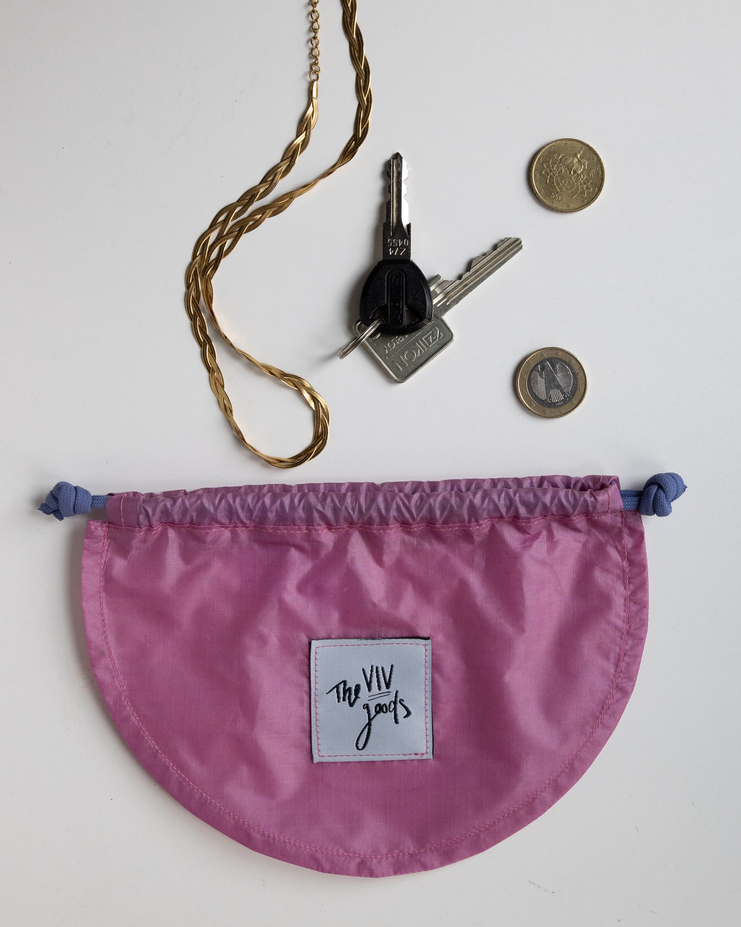 flat lay of drawstring pouch in light pink and purple with accessories that can fit inside bag