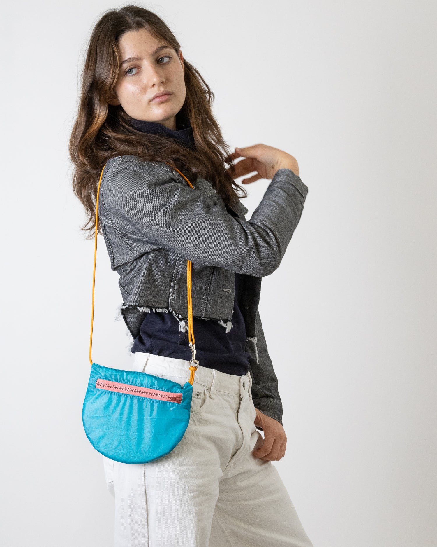 Model wears teal cross body bag with dusty rose zipper made from upcycled paraglider nylon U.BAG