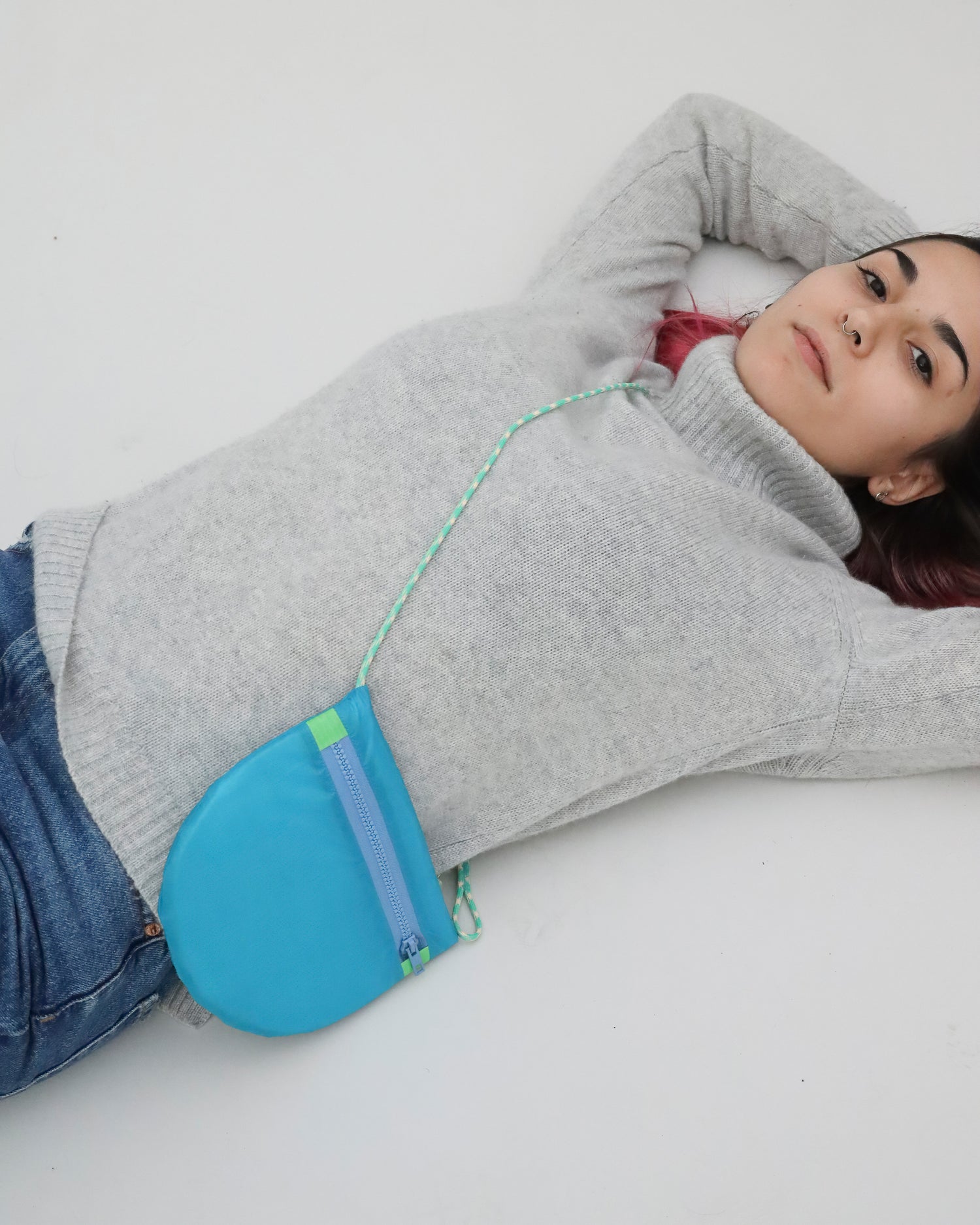Model wearing crossbody bag in turquoise and green made from recycled rip stop nylon